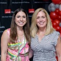 Two individuals pose indoors in front of a UTMB Health and John Sealy School of Medicine branded backdrop, with red, white, and gray balloon decorations on the side, wearing semi-formal attire.
