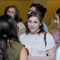 Several attendees stand in a group indoors, engaged in conversation, with multiple people visible in the background wearing semi-formal attire in a softly lit event space.