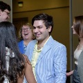 Several attendees stand indoors in a small group, engaged in conversation at a formal event, with individuals in semi-formal attire and a softly lit background in a reception setting.