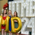 Three individuals stand indoors holding large gold “M” and “D” balloons in front of illuminated “UTMB 24” letters, with red, white, gold, and silver balloon clusters on both sides against a curtain backdrop. Provide your feedback on BizChat