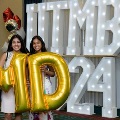 Two individuals stand indoors holding large gold “M” and “D” balloons in front of illuminated “UTMB 24” letters, with red, white, gold, and silver balloon clusters arranged on both sides against a curtain backdrop.