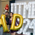 Two individuals stand indoors holding large gold “M” and “D” balloons in front of illuminated “UTMB 24” letters, with red, gold, silver, and white balloon clusters on each side against a curtain backdrop. Provide your feedback on BizChat