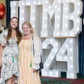 Two individuals stand together in front of illuminated “UTMB 2024” letters with red, white, and gold balloon decorations at an Alpha Omega Alpha Texas Alpha Chapter event.