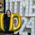 Individual stands in front of illuminated “UTMB 2024” display holding large gold “M” and “D” balloons with red, white, and gold decorations at an Alpha Omega Alpha Texas Alpha Chapter event.