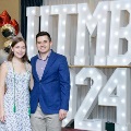 Two individuals stand together in front of illuminated “UTMB 2024” display, one wearing green honor cords, with red, white, and gold balloon decorations at an Alpha Omega Alpha Texas Alpha Chapter event.