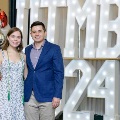 Two individuals stand together in front of illuminated “UTMB 2024” display, one wearing green honor cords, with red, white, and gold balloon decorations at an Alpha Omega Alpha Texas Alpha Chapter event.