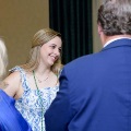 Individual wearing green honor cords engages in conversation with two others in a formal indoor setting during an Alpha Omega Alpha Texas Alpha Chapter event at UTMB.