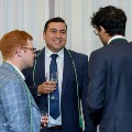 Four individuals wearing green honor cords stand in conversation while holding drinks in a formal indoor setting at an Alpha Omega Alpha Texas Alpha Chapter event at UTMB.