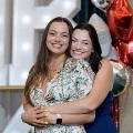 Two individuals stand closely together with one person’s arms around the other in front of illuminated “UTMB 2024” display with red, white, and gold balloon decorations at an Alpha Omega Alpha Texas Alpha Chapter event.