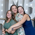 Three individuals stand closely together with one person’s arms around the others in front of illuminated “UTMB” letters and event decorations at an Alpha Omega Alpha Texas Alpha Chapter celebration.