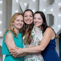 Three individuals stand closely together with arms around each other in front of illuminated “UTMB” letters and balloon decorations at an Alpha Omega Alpha Texas Alpha Chapter event.