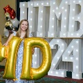 Individual holds large gold “M” and “D” balloons in front of illuminated “UTMB 2024” display with red, white, and gold balloon decorations at an Alpha Omega Alpha Texas Alpha Chapter event.