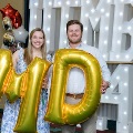 Two individuals stand in front of illuminated “UTMB 2024” display holding large gold “M” and “D” balloons with red, white, and gold decorations at an Alpha Omega Alpha Texas Alpha Chapter event.