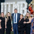 Seven individuals stand together in front of illuminated “UTMB 2024” display, with one wearing green honor cords, and red, white, and gold balloon decorations at an Alpha Omega Alpha Texas Alpha Chapter event.