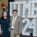 Two individuals stand together in front of illuminated “UTMB 2024” display, one wearing green honor cords, with red, white, and gold balloon decorations at an Alpha Omega Alpha Texas Alpha Chapter event.