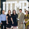 Seven individuals stand together in front of illuminated “UTMB 2024” display with red, white, and gold balloon decorations at an Alpha Omega Alpha Texas Alpha Chapter event.