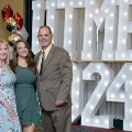 Three individuals stand together in front of illuminated “UTMB 2024” display with red, white, and gold balloon decorations at an Alpha Omega Alpha Texas Alpha Chapter event.