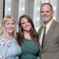 Three individuals stand together in front of illuminated “UTMB” letters at an Alpha Omega Alpha Texas Alpha Chapter event at the University of Texas Medical Branch.
