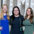 Three individuals stand together in front of illuminated “UTMB” letters, two wearing green honor cords, at an Alpha Omega Alpha Texas Alpha Chapter event.