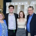 Four individuals stand together in front of illuminated “UTMB” letters with red, white, and gold balloon decorations at an Alpha Omega Alpha Texas Alpha Chapter event.