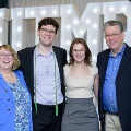Four individuals stand together in front of illuminated “UTMB” letters with decorative red, white, and gold balloons at an Alpha Omega Alpha Texas Alpha Chapter event.