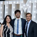 Three individuals stand together in front of illuminated “UTMB” letters with red, white, and gold balloon decorations at an Alpha Omega Alpha Texas Alpha Chapter event.