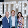 Three individuals stand together in front of illuminated “UTMB 2024” display with red, white, and gold balloon decorations at an Alpha Omega Alpha Texas Alpha Chapter event.
