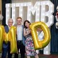 Three individuals pose in front of illuminated “UTMB” letters holding large gold “M” and “D” balloons, with red, white, and gold decorations at an Alpha Omega Alpha Texas Alpha Chapter event.