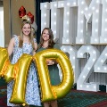 Two individuals stand in front of illuminated “UTMB 2024” display holding large gold “MD” balloons with red, white, and gold decorations at an Alpha Omega Alpha Texas Alpha Chapter event.