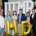 Six individuals pose in front of illuminated “UTMB” letters with large gold “MD” balloons and red, white, and gold decorations at an Alpha Omega Alpha Texas Alpha Chapter event.