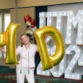 Individual holding large gold “M” and “D” balloons while standing in front of illuminated “UTMB” letters and “2024” display with decorative balloons at an Alpha Omega Alpha Texas Alpha Chapter event.