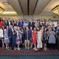 Approximately 40 attendees stand and sit together posing for a large group photo in a banquet hall with chandeliers and patterned carpet during the Alpha Omega Alpha Texas Chapter UTMB 2022 Fall Mixer.