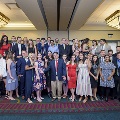 Approximately thirty attendees stand and sit together posing for a large group photo in a banquet hall with chandeliers and patterned carpet during the Alpha Omega Alpha Texas Chapter UTMB 2022 Fall Mixer.