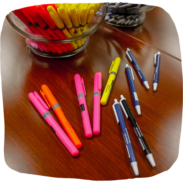 Highlighters and pens are spread out on a desk.