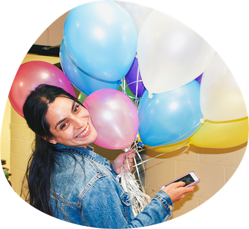 Girl with long hair smiles at camera while holding colorful balloons.