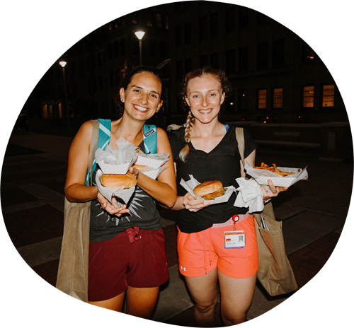 Two students stand side-by-side holding food at a student event.