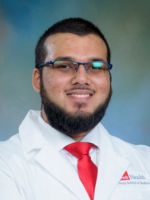 professional headshot of Syed Abdullah with short black hair and beard, wearing a red tie and whitecoat