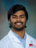 Professional headshot of Saketh Amasa with medium length brown hair, wearing a blue shirt under a whitecoat