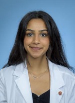 Professional headshot of Archie Patel with long black hair, wearing a black top under a whitecoat