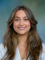 professional headshot of Puja Bhatia, with long highlighted brown hair, wearing a whitecoat