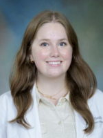 Professional headshot of Callie Jacob with medium length highlighted brown hair, wearing a cream colored top under a whitecoat