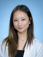 Professional headshot of Hannah Jung with medium length highlighted brown hair, wearing a black top under a whitecoat