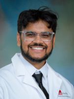 professional headshot of Manav Patel with with short dark hair, wearing glasses, a black tie, and a whitecoat