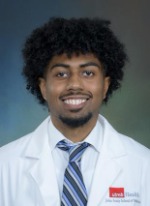 Professional headshot of Trisstan Weddington with medium length curly black hair, wearing a blue striped tiecurly under a whitecoat