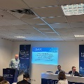 Conference room with a speaker presenting slides to an audience at a UTMB urogynecology fellowship session, with attendees seated and banners displayed near the podium.