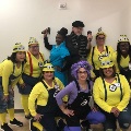 Group of fellowship participants posing indoors in Minions-themed costumes, including yellow shirts, suspenders, and character accessories, standing and kneeling together for a playful team photo.