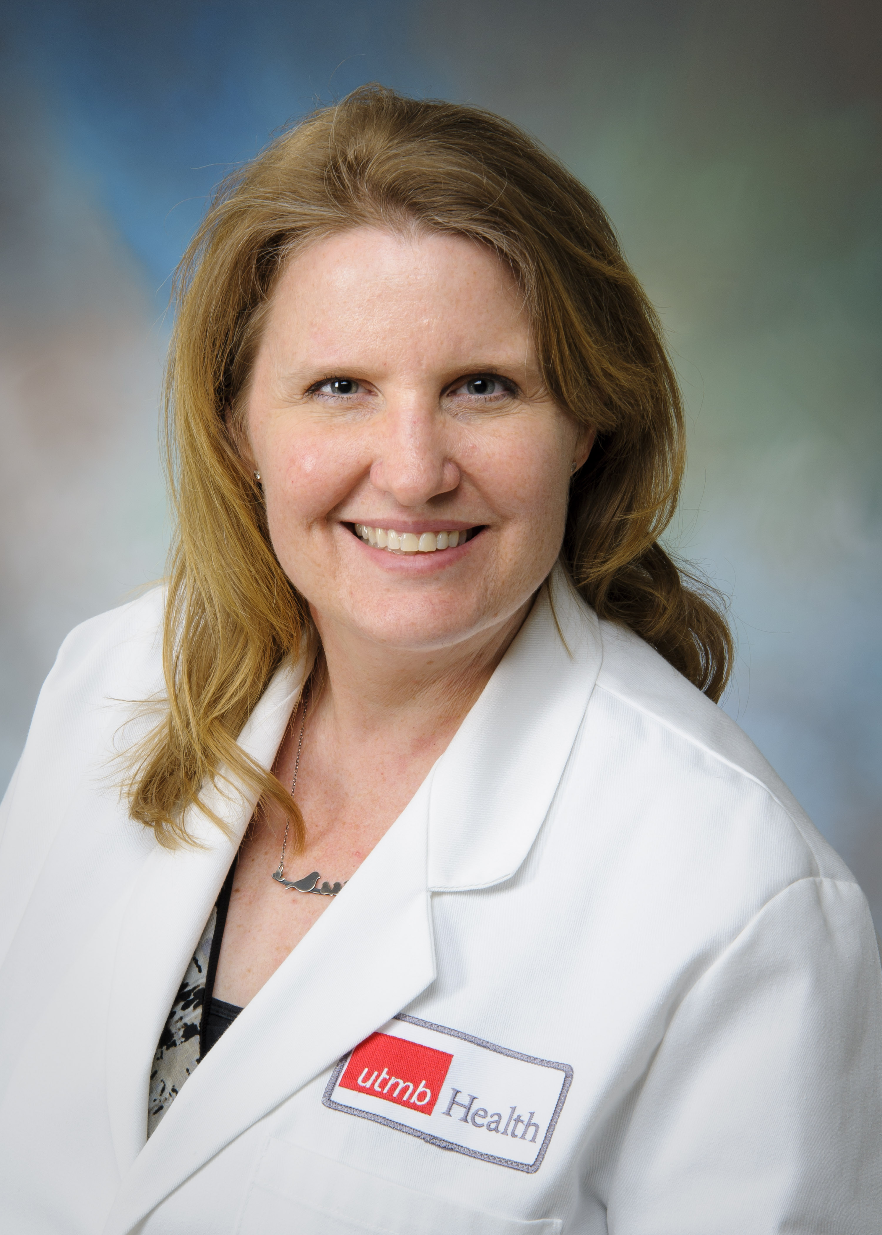 Studio headshot of a UTMB Health clinician in a white coat with a UTMB badge, facing forward against a soft gradient background; professional portrait used for Obstetrics and Gynecology faculty profile.