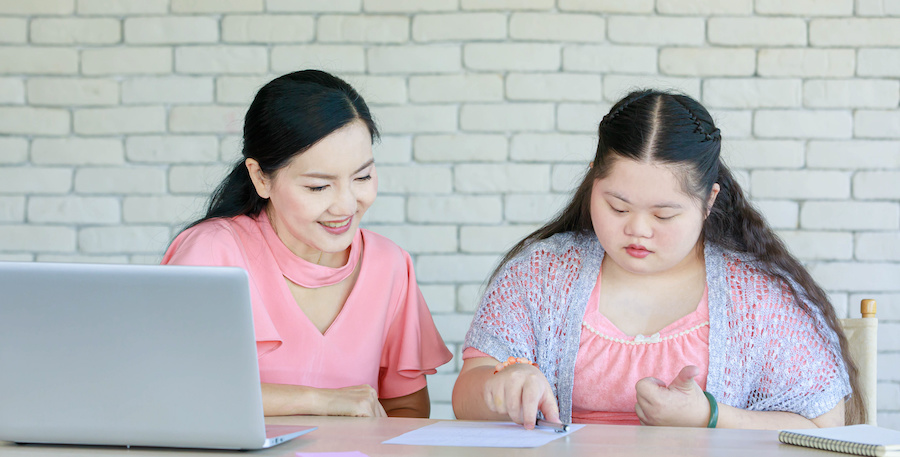 Asian mother and daughter sitting at a table with an open laptop and a sheet of paper