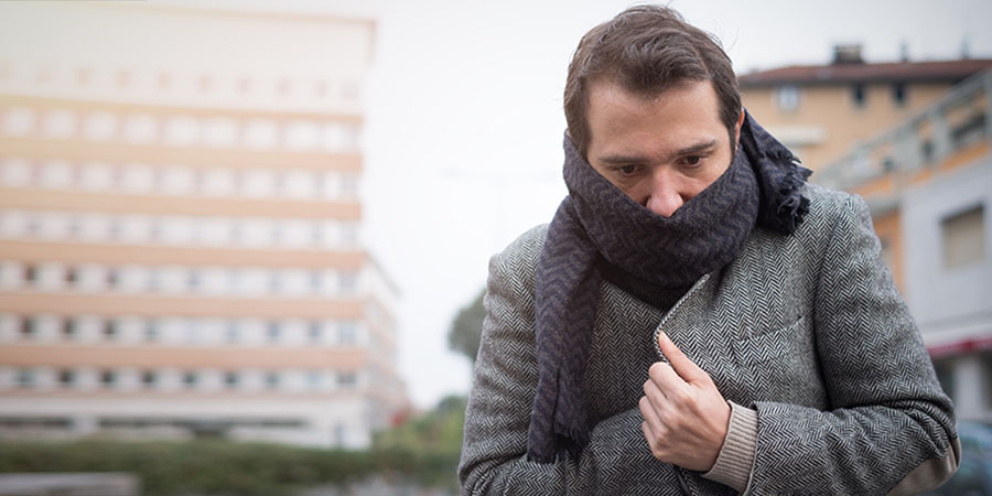 Man bundled up in a coat and scarf walking in an urban area