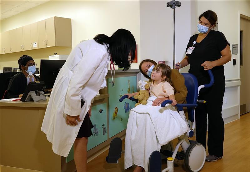 Hospital staff and a caregiver support a young patient in a wheelchair during a visit in a pediatric hospital unit